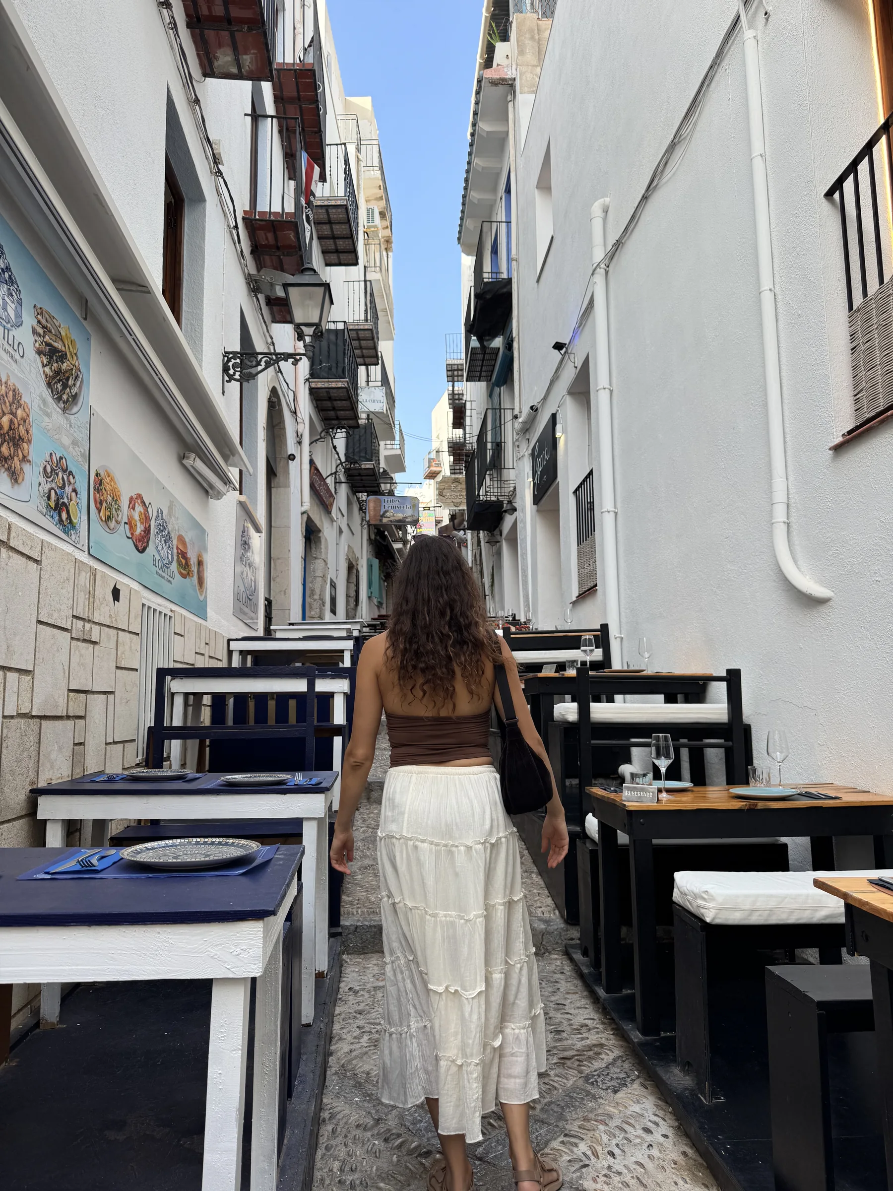 A traveller walking a narrow restaurant-lined street in the old town of Peñíscola.